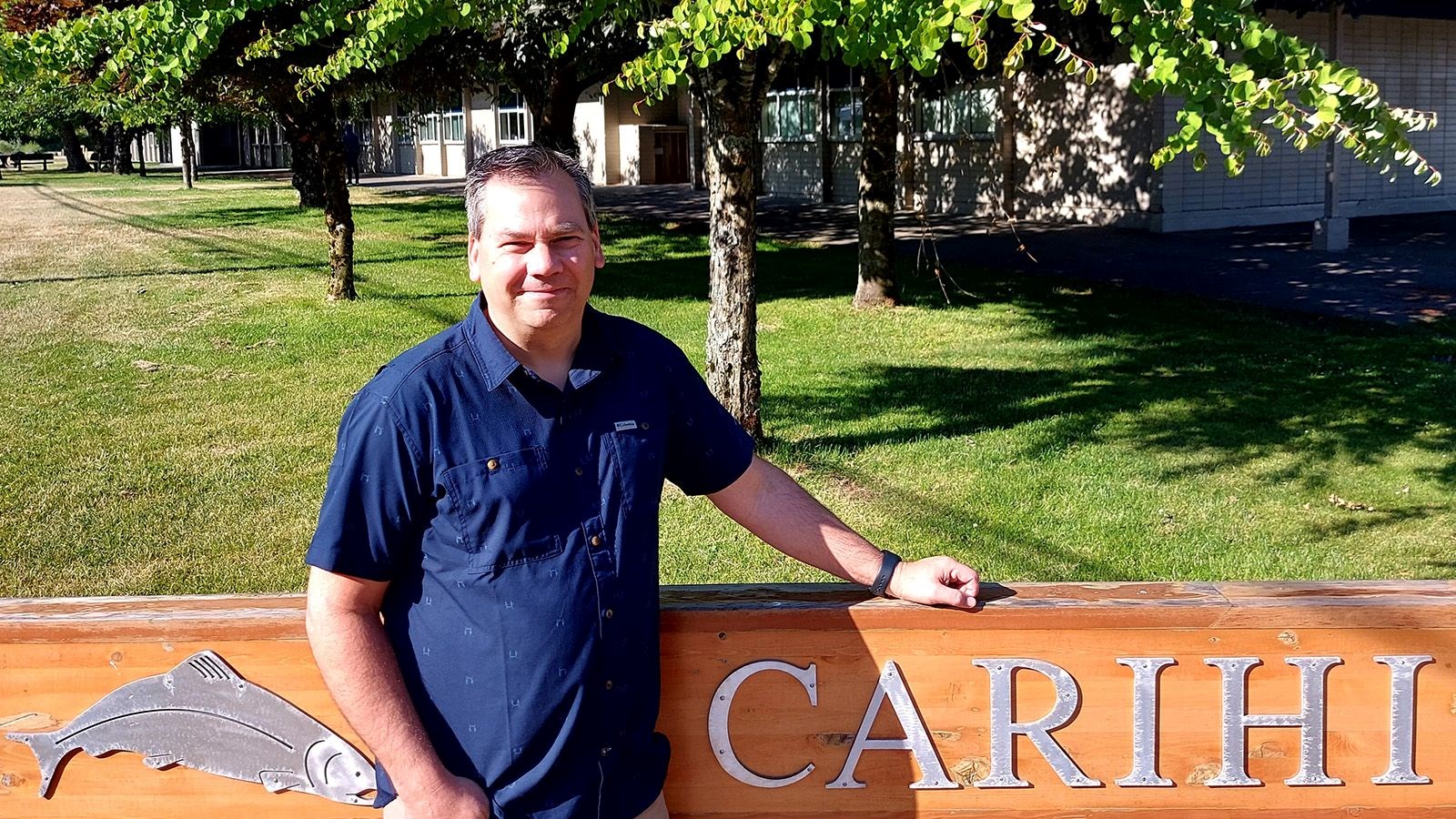 Teacher Bill Deagle standing in front of the school sign outside of Carihi Secondary.