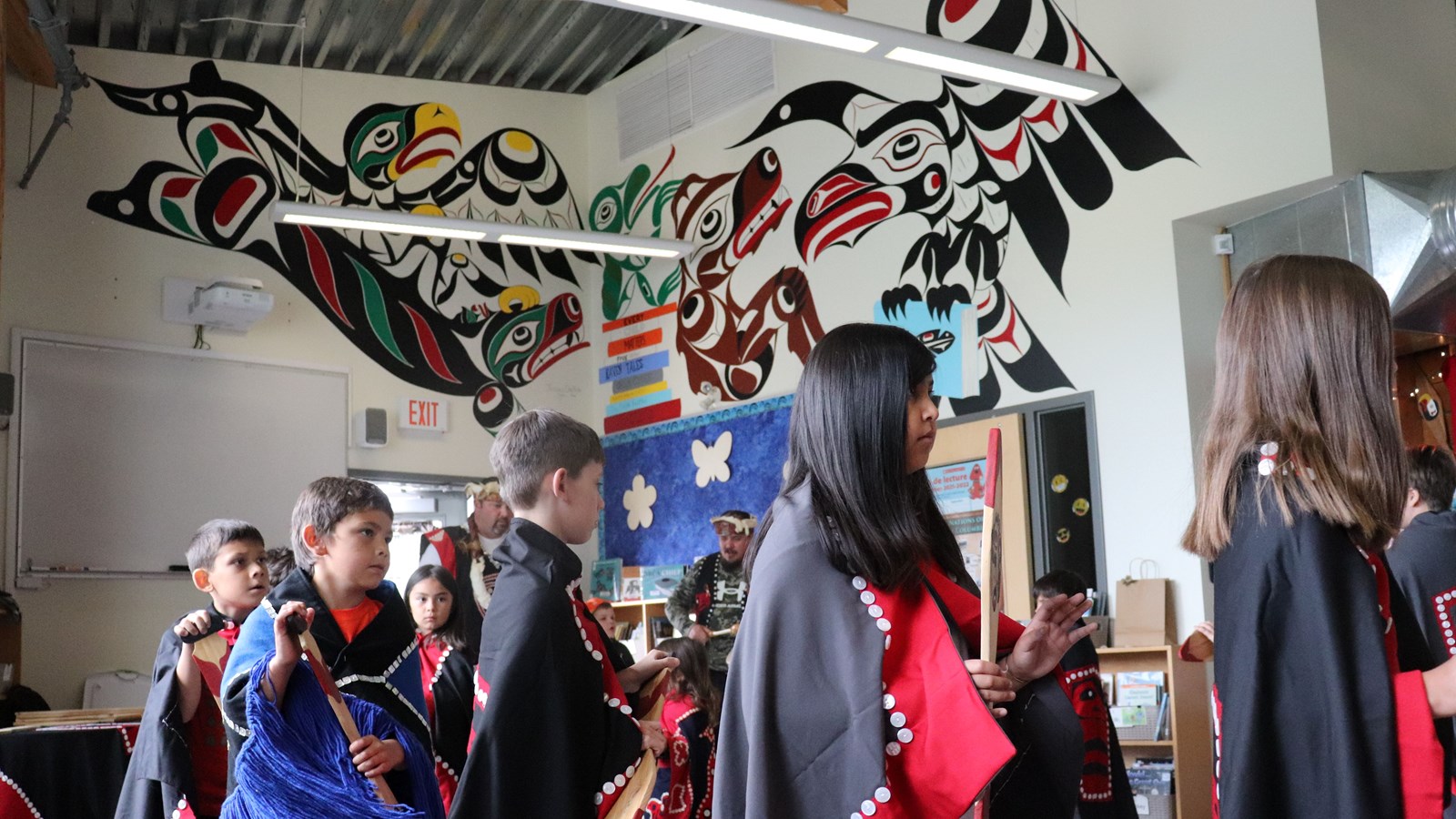 Students participating in the Paddle Dance in front of the full mural painted by Jessica Chickite.